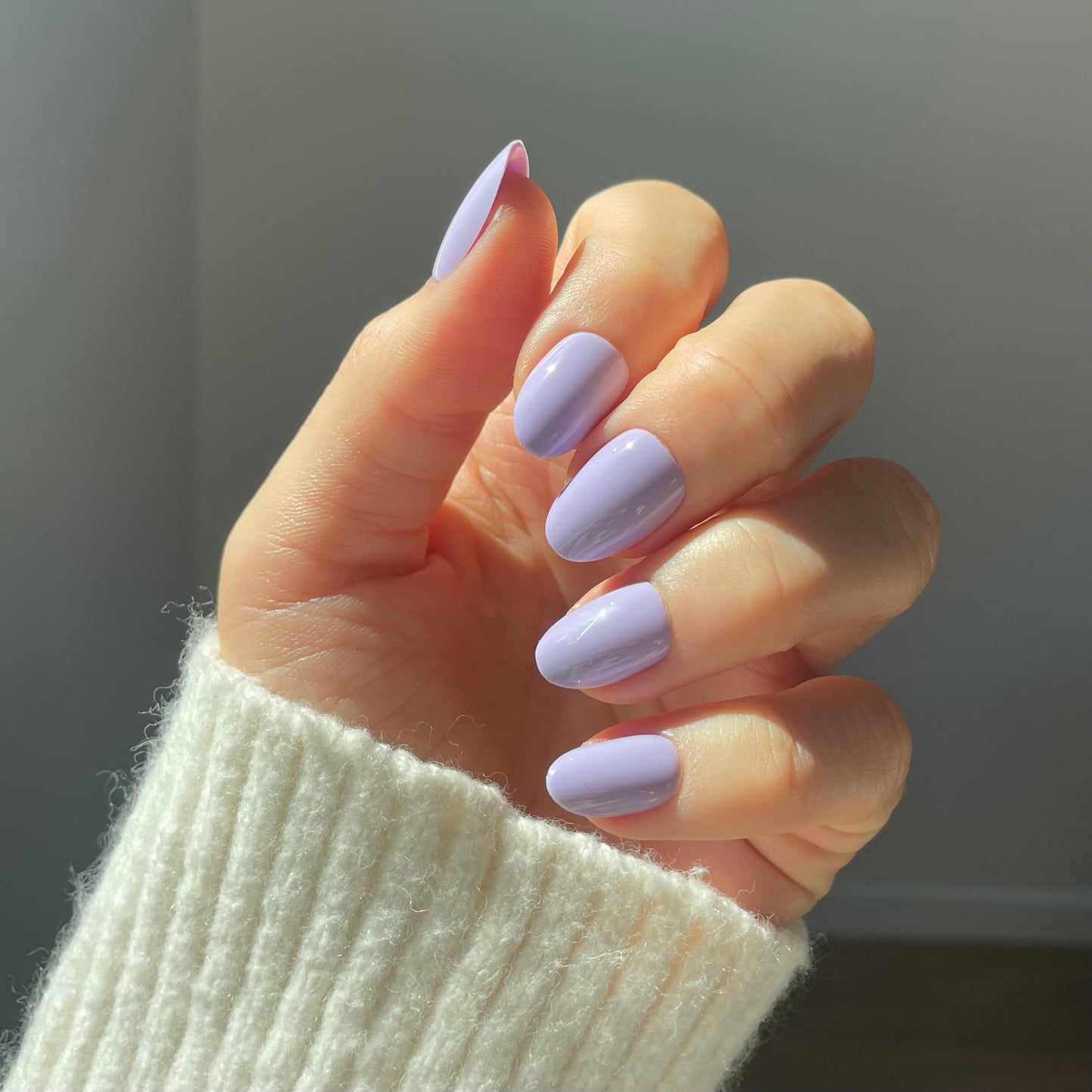 Womans hand wearing lilac press-on acrylic nails. Light purple salon quality