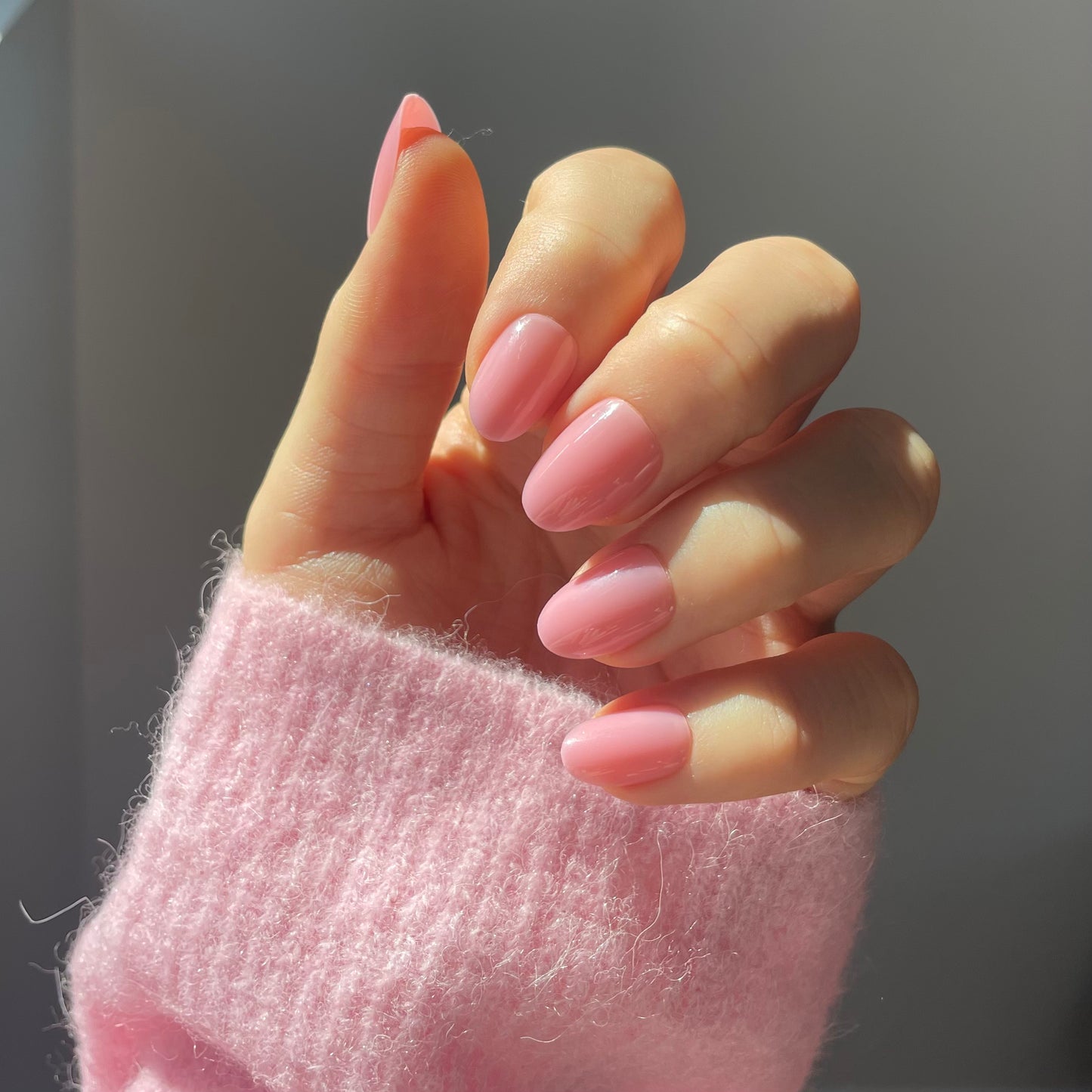 Womans hand wearing malibu short oval mid-pink press-on acrylic nails