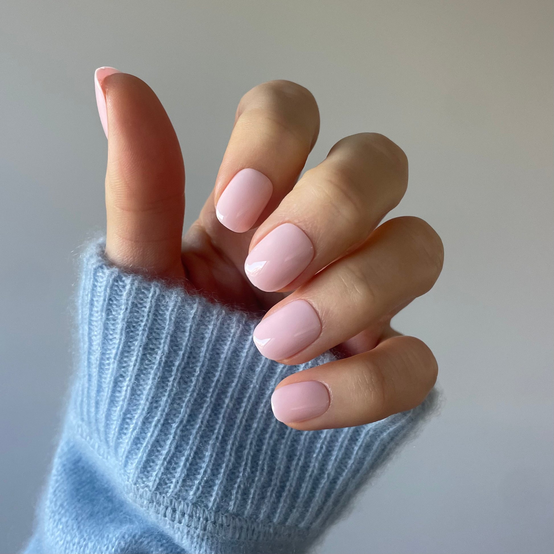 Womans hand with salon quallity Candy Claws pillow talk press-on acrylic nails in the palest pink. Removable and reusable