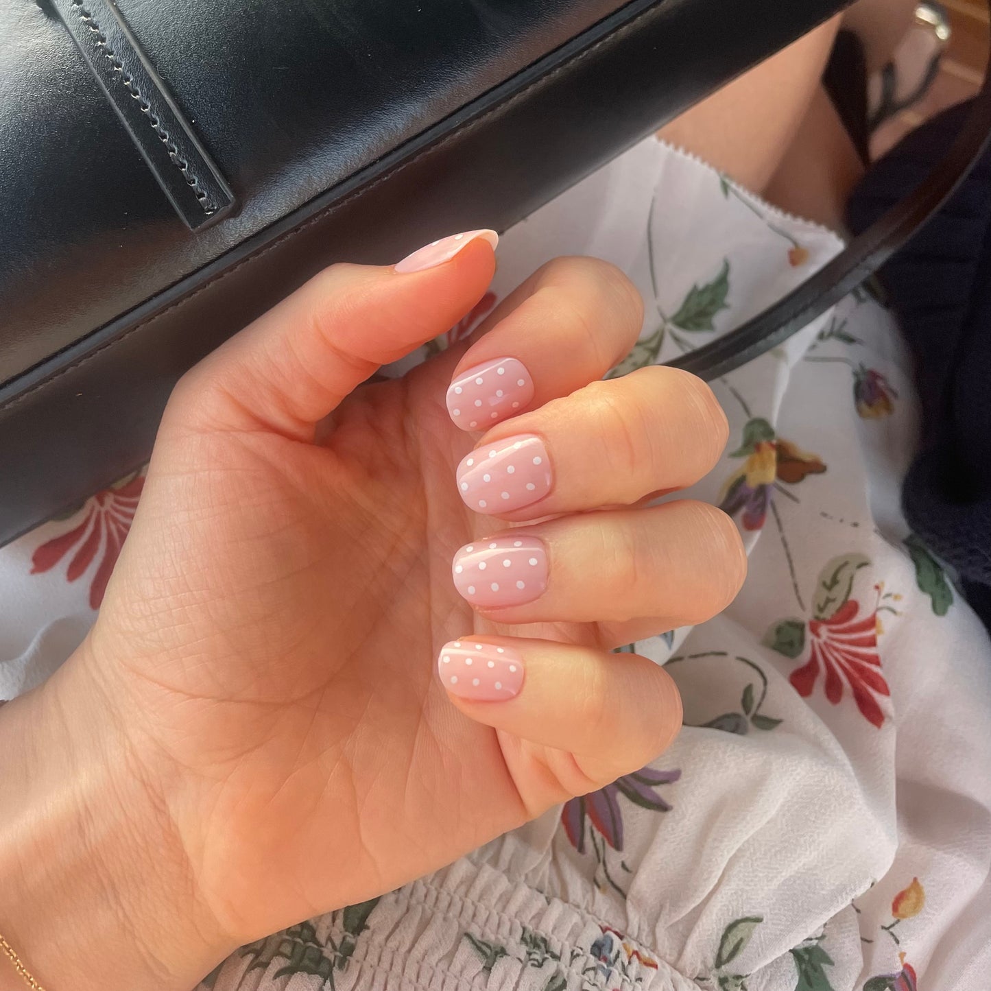 Womans hand with translucent pink polka dot press-on fake acrylic nails with white polka dots in the extra-short style
