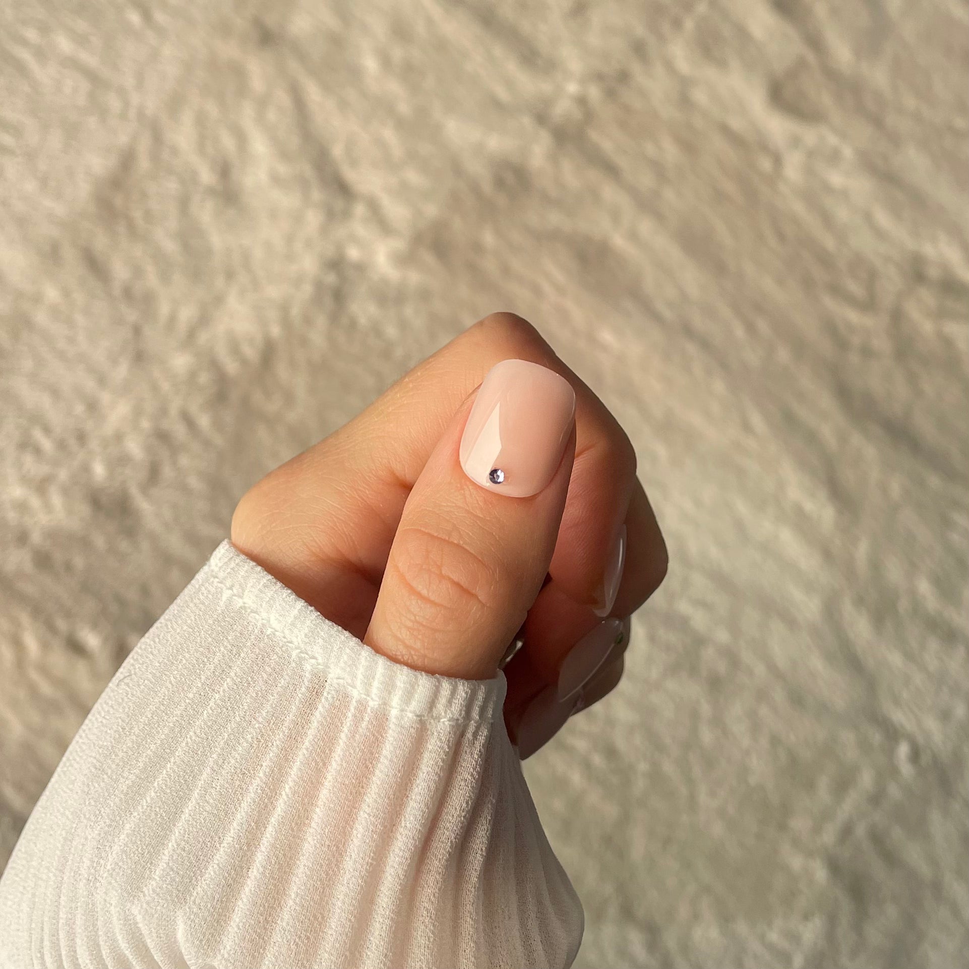 Woman's hand showing salon quality press on nail on the thumb. Pale pink (bare minimum) extra-short style with a gem at the base)