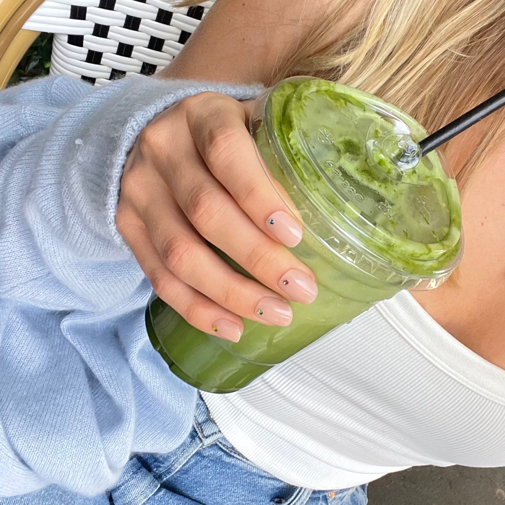 Woman's hand holding a smoothie with pink bare minimum fake nails with a gem on each one