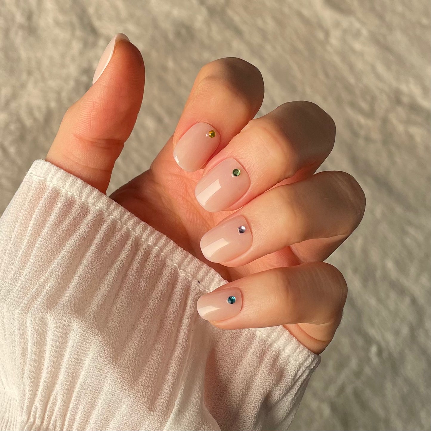 Woman's hand with Candy Claws gem and tonic press on nails. Bare minimum extra short nail style with gems on.