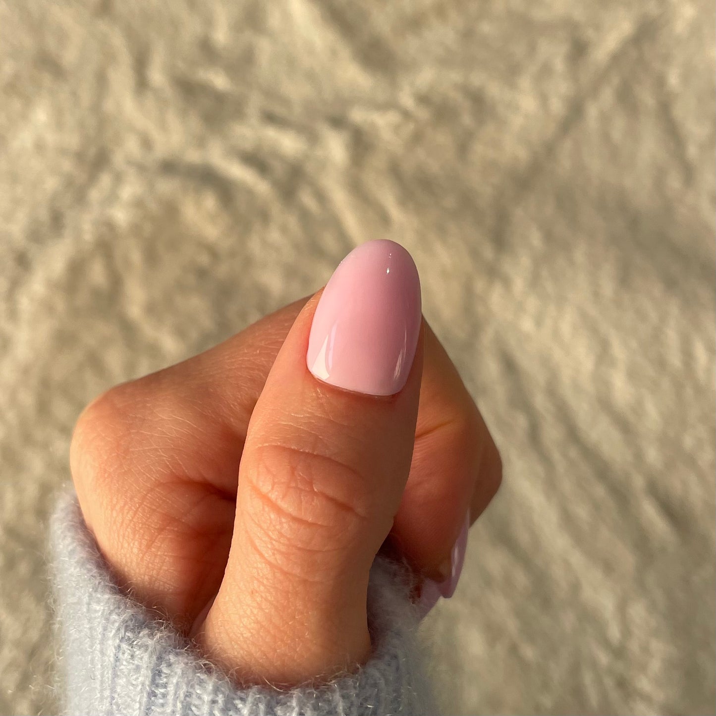 Womans thumb with Candy Claws fake acrylic press-on nail in lilac with a pink-lavender undertone. Removable