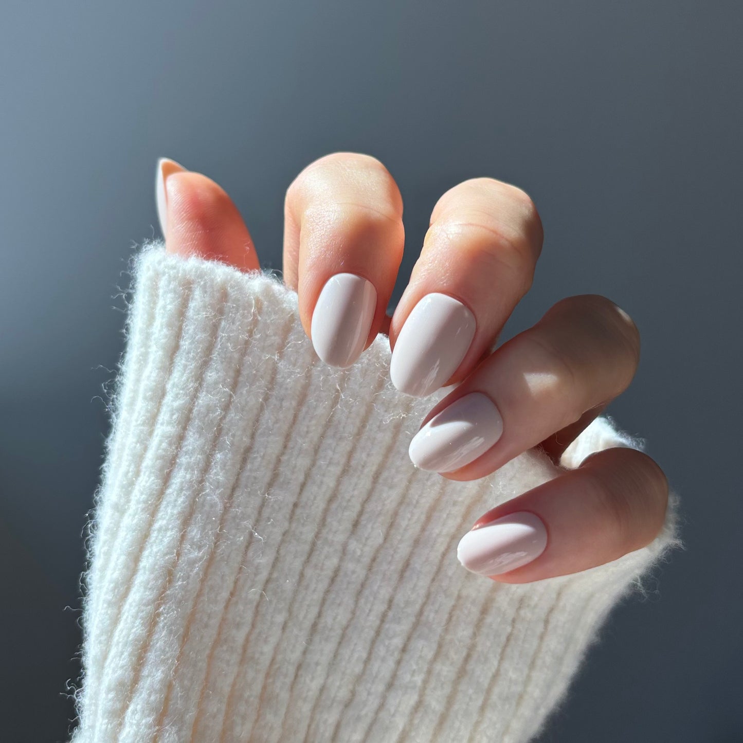 Womans hand showing pale elegant press-on acrylic nails in short oval style crema vanilla colour