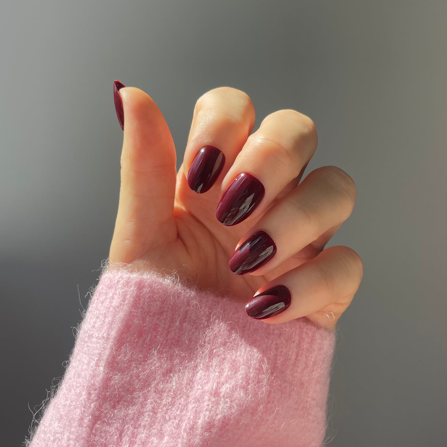 Womans hand wearing deep plum colourt fake nails from Candy Claws (sour grape short oval style). Salon quality reusable