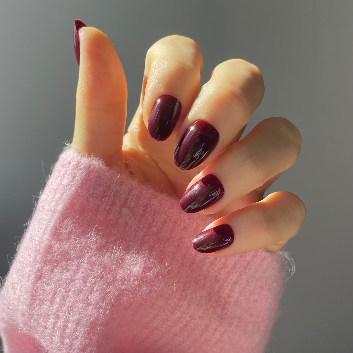 Womans hand wearing sour grape press-on acrylic nails in Candy Claws short oval style. Rich deep plum colour