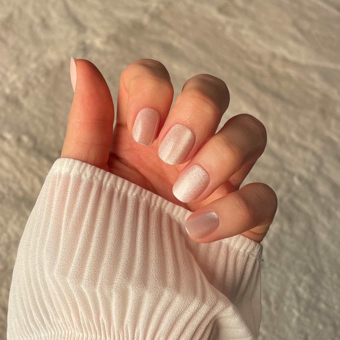 Womans hand showing salon quality pink glitter press-on fake nails in the extra-short style